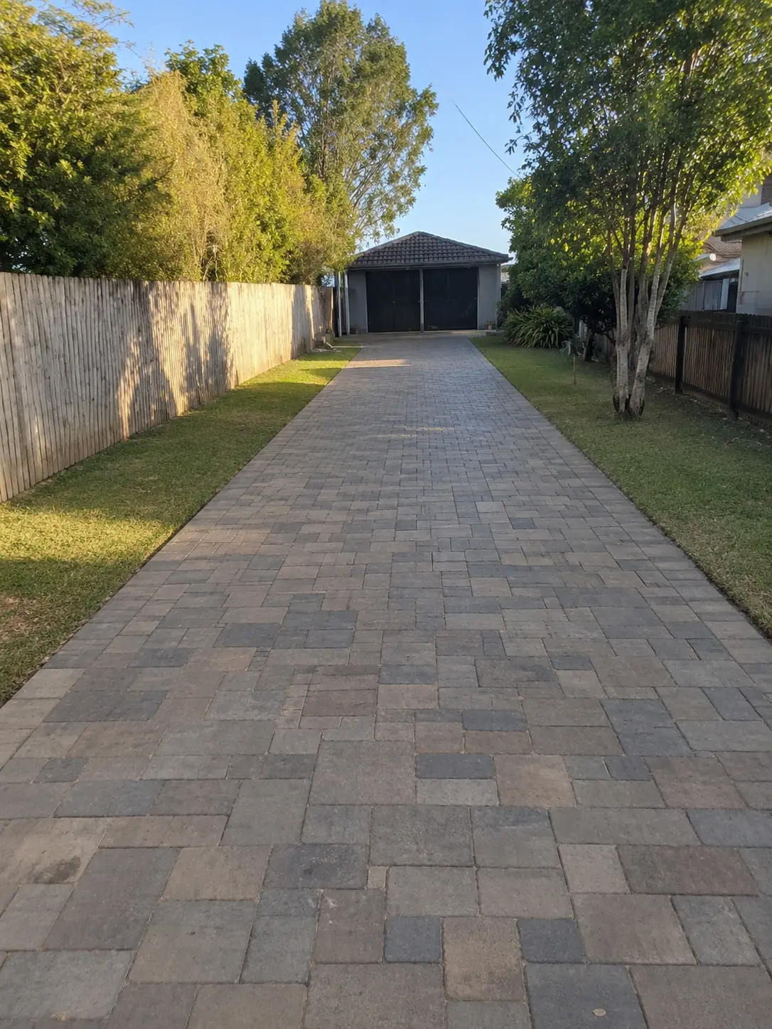 Long concrete paver driveway running between lawns to a rear garage, Cairns